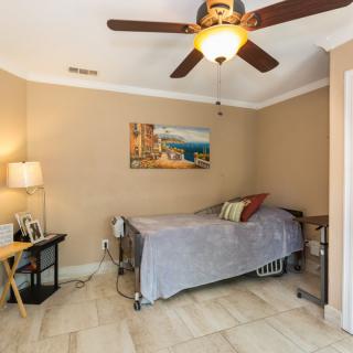 A cozy bedroom featuring a single bed and ceiling fan, with warm beige walls and decorative artwork.