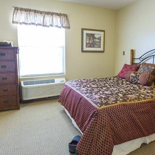 A cozy bedroom with a decorative bedspread and a dresser by the window.