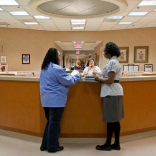 Two healthcare workers interacting at a hospital reception desk.