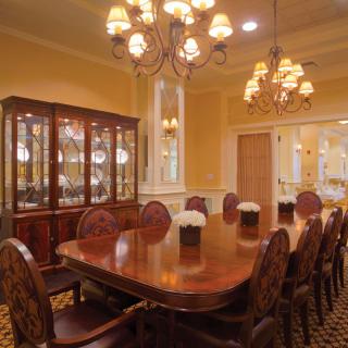 An elegant dining room featuring a large wooden table, upholstered chairs, and ornate chandeliers.
