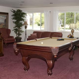A cozy game room featuring a pool table, leather seating, and large windows.