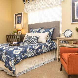 A cozy and well-decorated bedroom featuring a patterned bedspread, an orange armchair, and stylish nightstands with lamps.