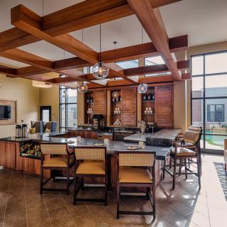 A spacious modern kitchen with wooden beams, an island counter, and bar stools, illuminated by natural light from large windows.