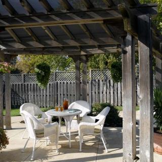 A sunny patio with wicker furniture under a pergola in a garden setting.