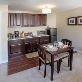 A compact kitchen and dining area with a small table set for two, featuring dark wood cabinets and modern appliances.