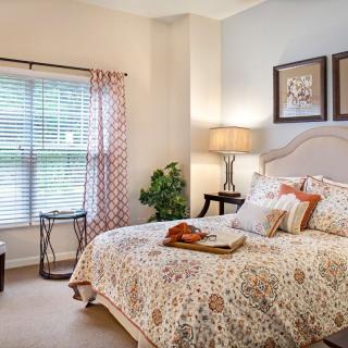 A cozy bedroom with a patterned bedspread, artworks on the wall, and natural light coming through the window.