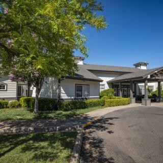 A well-maintained house with a driveway, surrounded by trees and landscaping under a clear blue sky.