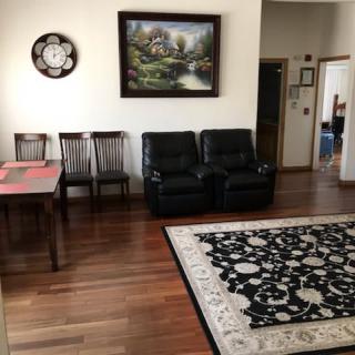 A cozy living room featuring a dining table, black leather sofa, and a decorative rug.