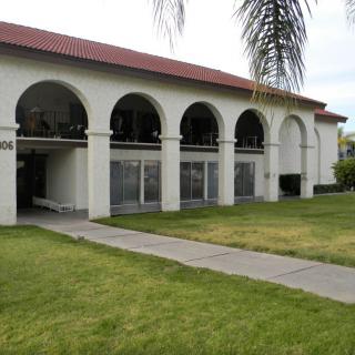 A building with arched windows and a well-maintained lawn, featuring a palm tree in the foreground.