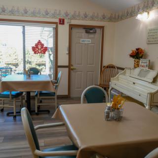 A cozy dining area with tables and chairs, featuring a white piano and decorative elements near the window.