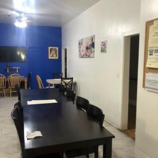A dining room with a long table, surrounded by chairs, featuring a blue accent wall and a TV.