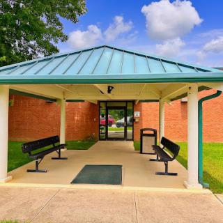 A welcoming entrance with a covered area, benches for seating, and lush green surroundings.