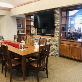 A cozy dining room featuring wooden furniture, a mounted television on a stone-accented wall, and decorative shelving.
