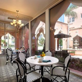 A cozy cafe with indoor seating and large arched windows overlooking a charming courtyard.