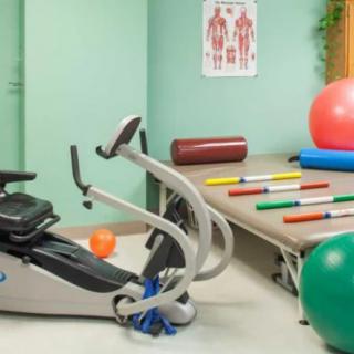 A well-equipped therapy room with a stationary bike, exercise balls, and various fitness mats.