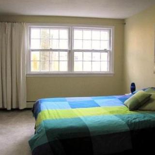 A simple bedroom with a colorful bedspread and large windows letting in natural light.