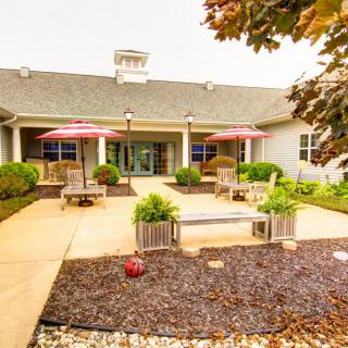 A charming outdoor patio area with benches, umbrellas, and well-maintained landscaping in front of a building.