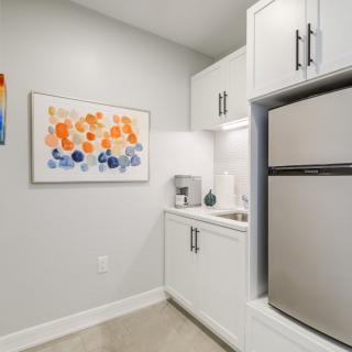A modern kitchen area with white cabinets, a refrigerator, and colorful artwork on the wall.
