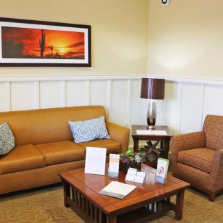 A cozy living room with a sofa, armchair, and a coffee table, decorated with wall art and a lamp.