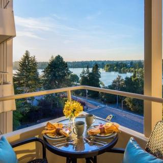 A scenic outdoor breakfast setup on a balcony overlooking a lake and trees on a sunny day.