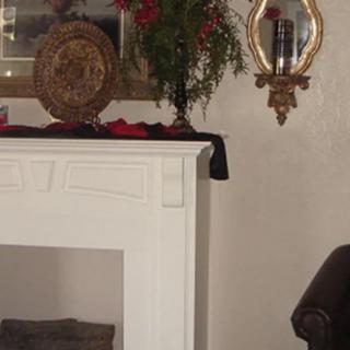 A traditional interior setting featuring a white fireplace mantel adorned with a decorative plate, a vase of flowers, and an ornate mirror hanging on the wall.
