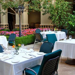 Outdoor restaurant seating area with elegantly set tables surrounded by lush greenery and vibrant flowers.