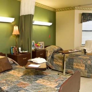 A hospital room with twin beds and a curtain divider, featuring green walls and lamps on nightstands.