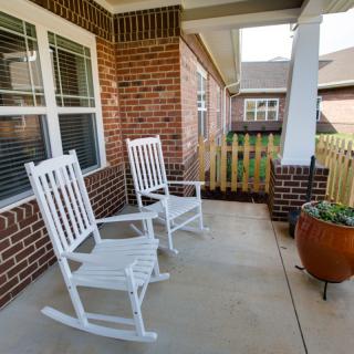 A cozy porch featuring two white rocking chairs against a brick wall, perfect for relaxation.