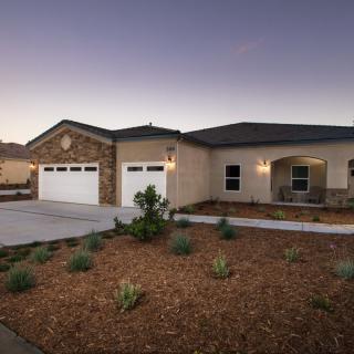 A modern single-story house with a two-car garage and landscaped front yard at dusk.