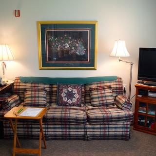 A cozy living room with a plaid sofa, lamps on either side, and a TV stand.
