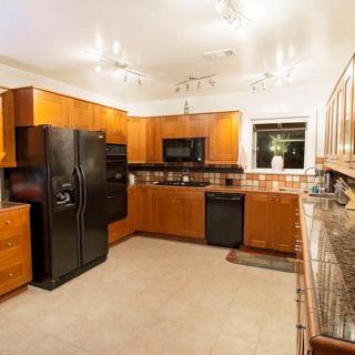 A modern kitchen with wooden cabinets, black appliances, and tile flooring, illuminated by bright lighting.