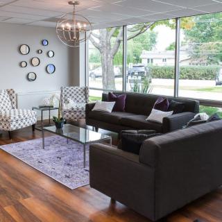 A modern living room with large windows, featuring stylish sofas and decorative wall pieces.