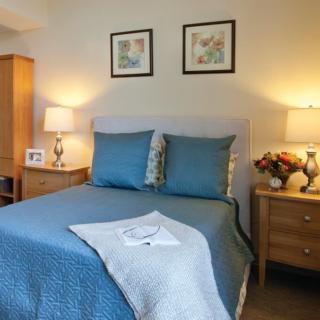 A cozy bedroom with blue bedding, flanked by wooden nightstands and illuminated by warm lamps, features artwork above the bed.