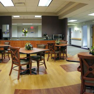 A cozy dining area featuring wooden tables, chairs, and decorative flowers, complemented by a kitchenette in the background.