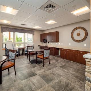 A modern office meeting room with tables and chairs, featuring a large window providing natural light.