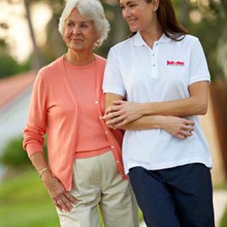A caregiver and an elderly woman enjoying a walk together outdoors.