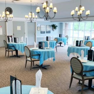 A brightly lit dining area with round tables covered in blue tablecloths and elegant chandeliers hanging from the ceiling.