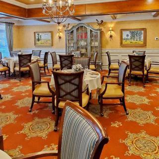 An elegant dining room with neatly arranged tables and chairs, featuring a warm carpet and decorative chandelier.