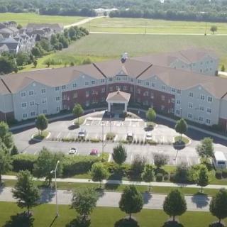 Aerial view of a large residential building with a surrounding landscape of trees and a parking lot.