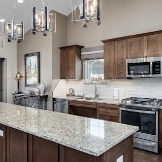 A modern kitchen featuring granite countertops, wood cabinetry, and stainless steel appliances, illuminated by stylish light fixtures.