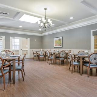 A spacious and elegantly designed dining room with multiple tables and chairs, featuring a chandelier and wooden flooring.