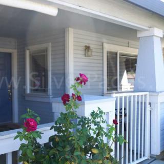 A view of a porch with blooming flowers, white railing, and a blue door.