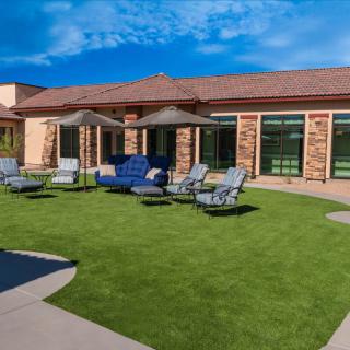 A sunny patio area with seating arrangements and umbrellas on a well-maintained lawn.