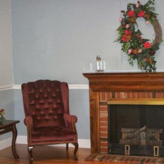 A cozy living room featuring a tufted armchair and a rustic fireplace adorned with a seasonal wreath.