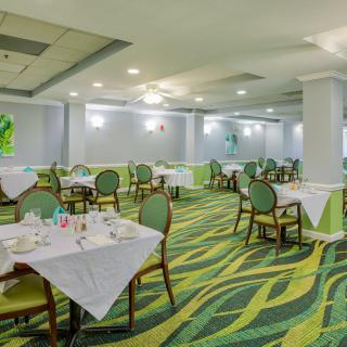 A spacious restaurant interior with neatly arranged tables and chairs, featuring a vibrant carpet design.