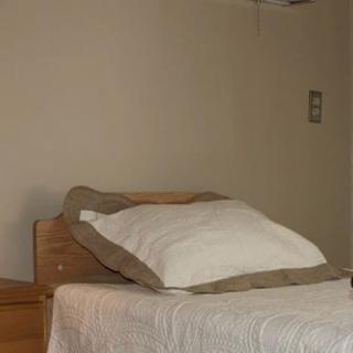 A minimalist bedroom featuring a neatly made bed with a white quilt and pillow.