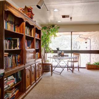 A cozy study room with a wooden bookshelf, desk, and large window view.