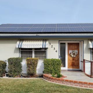 A charming residential house featuring solar panels on the roof, surrounded by well-maintained landscaping.