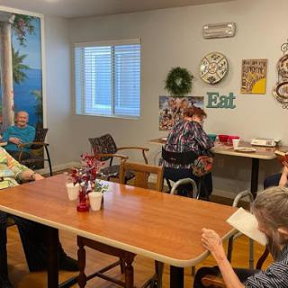 A cozy activity room in a senior center, featuring residents engaged around tables with decorative elements on the walls.