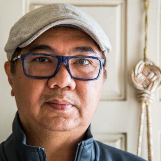 A man wearing glasses and a hat, standing indoors.